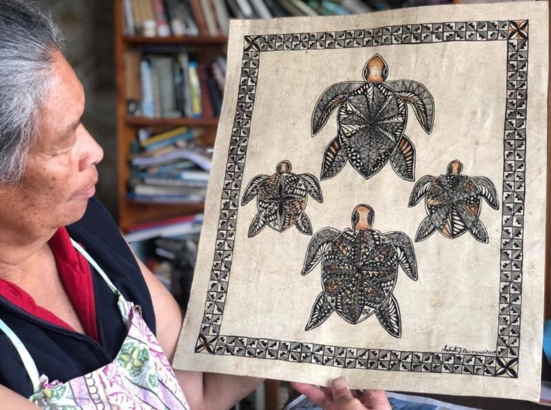 Artist Sulieti Fieme'a Burrows holding up one of her tongan tapa artworks featuring a kupesi border with a family of four turtles.